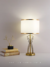 Abajur Cidonia moderno dourado com cúpula branca em uma mesa ao lado de livros decorativos. Lustres Gênesis Site online venda de Lustres e Iluminação