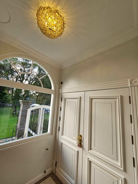 Plafon de cristal iluminando uma entrada com portas brancas e janela arqueada. Lustres Gênesis loja online de Lustres e Iluminação Decorativa