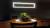 Lustre pendente de LED moderno dourado iluminando uma sala com mesa de jantar e planta decorativa. Lustres Gênesis Site online venda de Lustres e Iluminação Decorativa