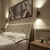 Arandela Moderna Rudá Café Fosco instalada ao lado de uma cama em um quarto decorado. Arandela Moderno Botton de LED Dourada da SkyLight, modelo SKY-3111AR-DO, com design circular e detalhes texturizados. Lustres Gênesis Site online venda de Lustres e Ilu