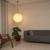 Luminária de teto pendente em forma de esfera com acabamento em mármore, iluminando uma sala com sofá cinza e planta decorativa. Lustres Gênesis loja online de Lustres e Iluminação Decorativa. 