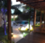 Luminária de Chão Meia Esfera Soleil Branca iluminando área externa com piscina e palmeiras. Lustres Gênesis loja online de Lustres e Iluminação Decorativa