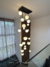 Lustre pendente Cosmos Jabuticaba com 21 globos leitosos brancos em ambiente de pé direito duplo alto e escadas de casas modernas teto alto, escada preta e cortina grande. Lustres Gênesis