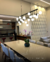 Luminária de teto pendente com 23 globos leitosos sobre mesa de jantar moderna em ambiente interno. Lustres Gênesis loja online de Lustres e Iluminação Decorativa