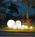 Luminária de chão em formato de esfera Soleil branca iluminando jardim externo à noite. Lustres Gênesis loja online de Lustres e Iluminação Decorativa