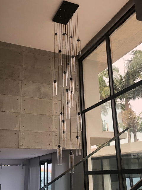 Lustre pendente moderno Dunáh com 21 tubos de vidro fumê instalado em hall com pé direito duplo, destacando design industrial e elegante para ambientes amplos.