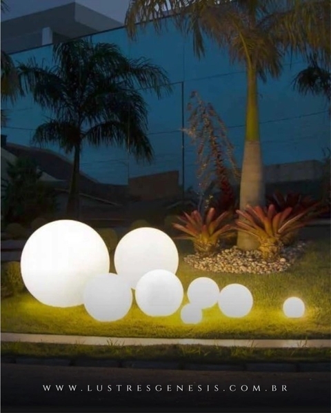 Luminária de chão em formato de esfera Soleil branca iluminando jardim externo à noite. Lustres Gênesis loja online de Lustres e Iluminação Decorativa