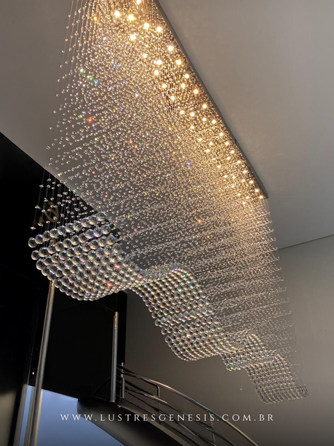 Lustre grande de cristal modelo Onda, fabricado sob medida pela Lustres Gênesis, instalado em pé direito duplo acima de uma escada moderna.