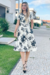 Vestido midi piquet branco com estampa floral, modelo Thais, usado por uma mulher em ambiente iluminado.