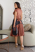 Modelo usando um vestido midi plissado em cirrê, com parte superior marrom e saia preta, em um ambiente moderno.