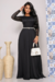 Vestido longo preto plissado em crepe preto com detalhes de renda nas mangas, modelado por uma mulher em ambiente decorado.