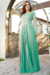 Vestido longo plissado em crepe na cor verde, com renda nas mangas e detalhes de cinto, posicionado em um ambiente ao ar livre.