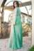 Vestido longo plissado em crepe na cor verde, com renda nas mangas e detalhes de cinto, posicionado em um ambiente ao ar livre.