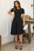 Modelo usando vestido midi preto de malha lese, com mangas bufantes, em ambiente elegante.