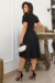 Modelo usando vestido midi preto de malha lese, com mangas bufantes, em ambiente elegante.