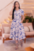 Modelo usando um vestido midi branco com estampa floral em tons de azul, com mangas curtas, em um ambiente moderno e aconchegante.