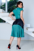 Modelo usando um vestido midi plissado em cirrê, com parte superior verde e saia em tons de verde e preto, posando em ambiente moderno.
