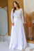 Modelo usando um vestido longo plissado em crepe branco com detalhes em renda e mangas longas.