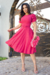 Modelo usando um vestido midi pink com mangas bufantes e detalhes em malha lese, segurando uma bolsa de flores, em um ambiente externo.