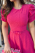 Modelo usando um vestido midi pink com mangas bufantes e detalhes em malha lese, segurando uma bolsa de flores, em um ambiente externo.