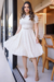 Mulher usando um vestido midi de malha lese na cor Off White, com detalhes em renda. O vestido tem mangas curtas e um cinto na cintura, enquanto ela está em um ambiente moderno e iluminado.