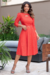 Modelo usando vestido midi vermelho com mangas 3/4 e detalhe em malha lese, posando em ambiente externo.