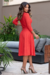 Modelo usando vestido midi vermelho com mangas 3/4 e detalhe em malha lese, posando em ambiente externo.