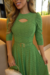 Modelo usando um vestido midi verde de manga 3/4, com detalhes em malha lese e cinto, em um ambiente elegante.