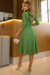 Modelo usando um vestido midi verde de manga 3/4, com detalhes em malha lese e cinto, em um ambiente elegante.