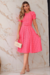 Vestido midi rosa de malha lese, com mangas bufantes e cinto na cintura, posando em um ambiente elegante.