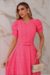 Vestido midi rosa de malha lese, com mangas bufantes e cinto na cintura, posando em um ambiente elegante.