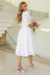 Modelo usando vestido midi branco de malha lese com mangas 3/4, segurando um buquê de flores.