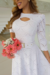 Modelo usando vestido midi branco de malha lese com mangas 3/4, segurando um buquê de flores.