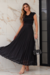 Mulher posando com um elegante conjunto de cropet e saia plissada preto com detalhe em floral na barra, em um ambiente sofisticado.