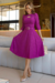 Mulher usando um vestido midi Fúcsia com manga 3/4 e detalhe na cintura, em ambiente moderno.
