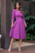 Vestido midi cor Fúcsia com mangas 3/4 e detalhe de recorte na cintura, usado por uma mulher em ambiente externo com plantas ao fundo.