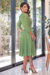 Vestido midi verde com manga 3/4, detalhe em faixa na cintura e recorte no decote, em ambiente iluminado.