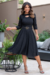 Modelo usando um vestido midi preto de manga 3/4, com detalhe em malha lese e cinto, em um ambiente externo.