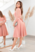 Modelo vestindo um elegante vestido midi rosê com detalhes em renda nas mangas, em um ambiente claro e moderno.