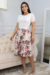 Modelo usando um vestido midi branco floral em piquet com renda, mangas curtas e saia rodada, em um ambiente interno elegante.