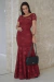 Modelo usando vestido longo rendado modelo sereia na cor marsala, com detalhes em renda e saia ajustada, segurando uma bolsa preta.