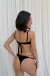 Mujer posando de espaldas con bikini Duetto Zebra color negro, con detalles de tiras regulables y diseño superpuesto. Fondo blanco liso.