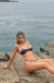 Mujer usando bikini Duetto Polka Dots Cielo con estampado de lunares y detalles en celeste, sentada sobre rocas frente al mar.