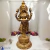 Escultura de Lakshmi em metal dourado, representando a deusa da riqueza e prosperidade, com flores ao fundo.
