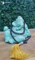 Estátua de Ganesha em tom verde, adornada com colares e uma franja dourada, em um fundo natural.