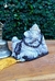 Estátua de Ganesha deitado com detalhes em relevo, decorada com um colar de contas escuras, ao lado de um sino em metal, sobre uma mesa de madeira.