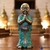 Estátua de Buda em posição de oração, com vestes azul-turquesa e detalhes dourados, em ambiente sereno.