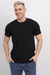 Hombre sonriente usando una remera básica de lycra negra, con pantalones de mezclilla, en un fondo blanco.