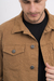 Detalle de una chaqueta gabardina de color camel con botones metálicos, usada por un hombre que se muestra en primer plano.