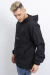 Anorak rompevientos negro con capucha y tensor lateral en la cintura, usado por un modelo masculino que mira hacia abajo.